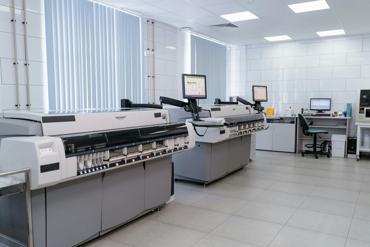 Modern large industrial printers with computer monitors in a clean, bright printing room .